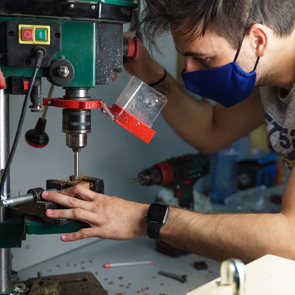 Man operating a drill press in a workshop, focusing on precision work with safety measures in place, relevant to electroplating and manufacturing processes.